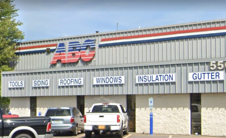 ABC Supply branch storefront with the red and blue ABC Supply signage and category signs for Tools, Siding, Roofing, Windows, Insulation, and Gutter along the front facade, with contractor pickups and SUVs parked in the customer lot